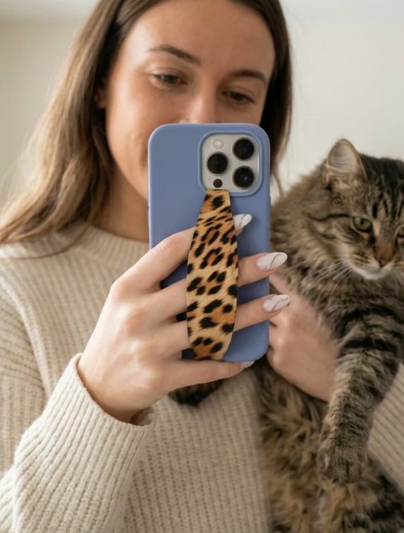 Woman holding a blue phone with a leopard print strap next to her tabby cat