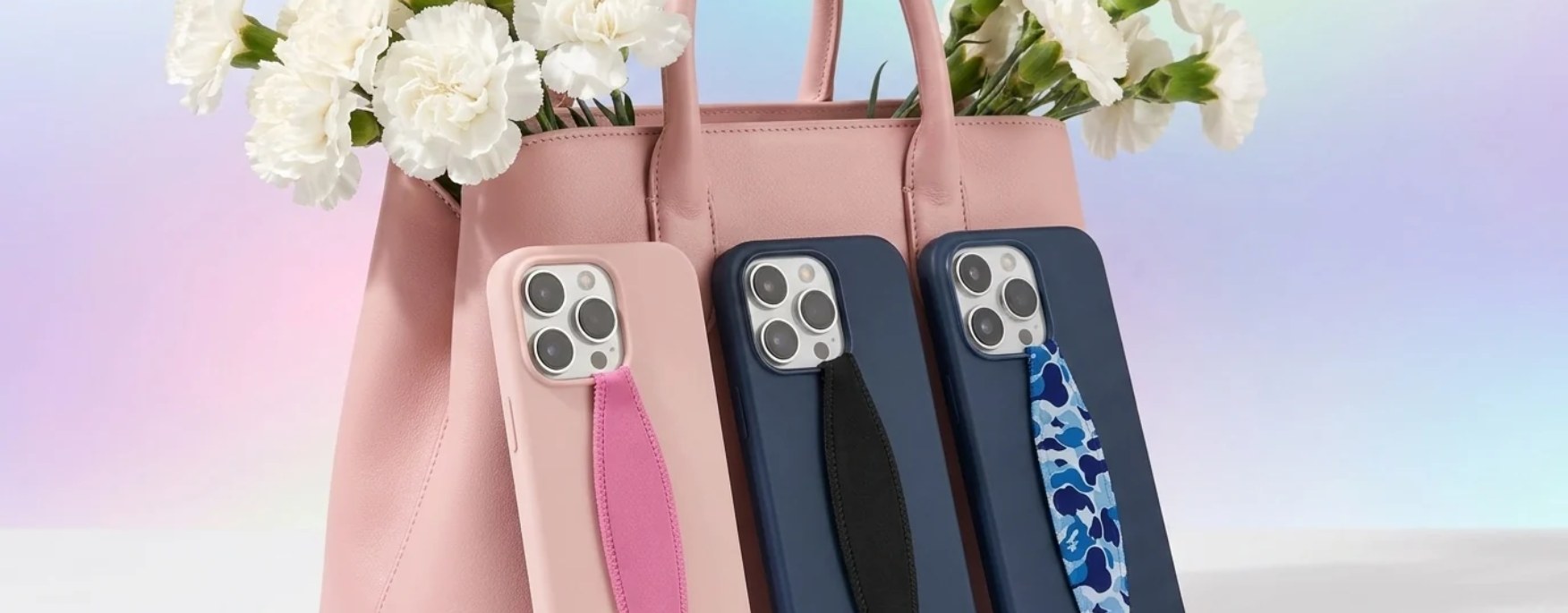 Pink, black and blue camo grip straps on pink and navy phone cases in front of a pink handbag with white carnations